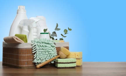 Image of Eco-friendly cleaning products and eucalyptus branches on wooden table against light blue gradient background, space for text