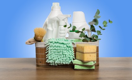 Eco-friendly cleaning products and eucalyptus branches on wooden table against light blue gradient background