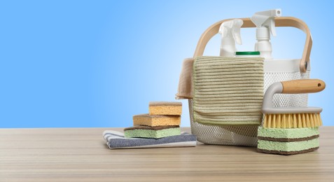 Image of Eco-friendly cleaning products on wooden table against light blue gradient background, space for text