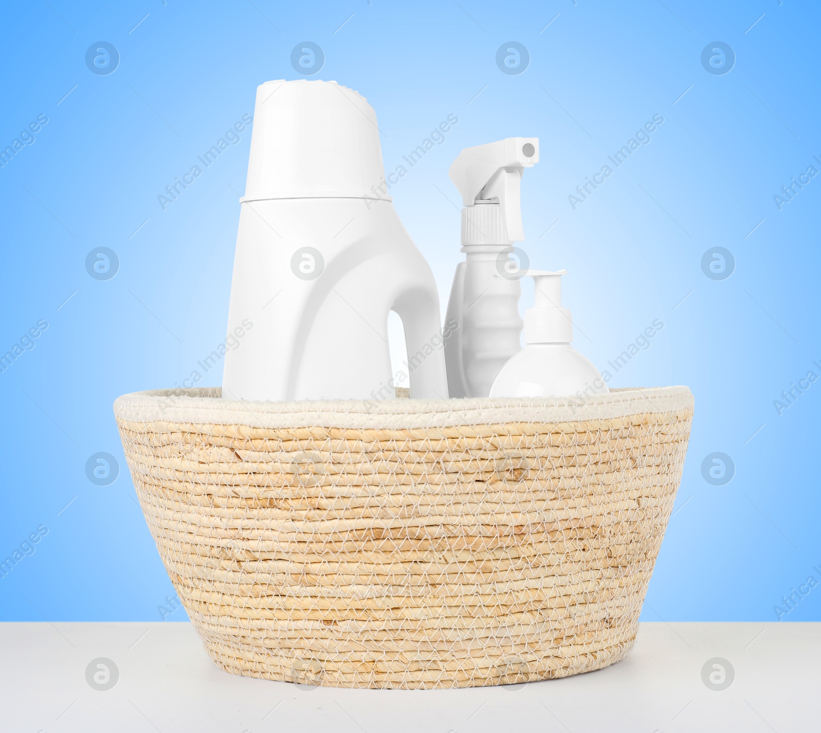 Image of Eco-friendly cleaning products in wicker basket on white table against light blue gradient background