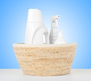 Image of Eco-friendly cleaning products in wicker basket on white table against light blue gradient background