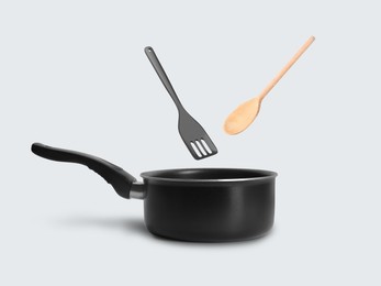 Image of Slotted spatula and wooden spoon in air over saucepan on white background