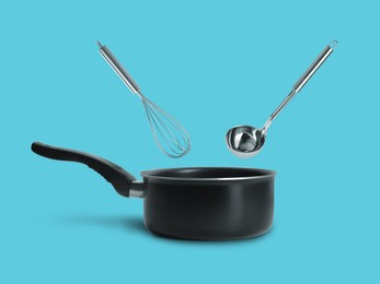 Image of Ladle and whisk in air over saucepan on light blue background