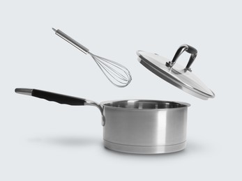 Image of Lid and whisk in air over saucepan on white background