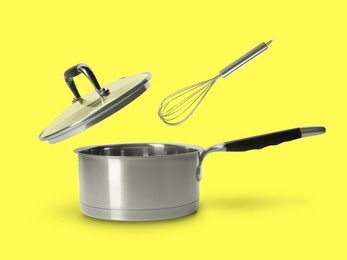 Image of Lid and whisk in air over saucepan on yellow background