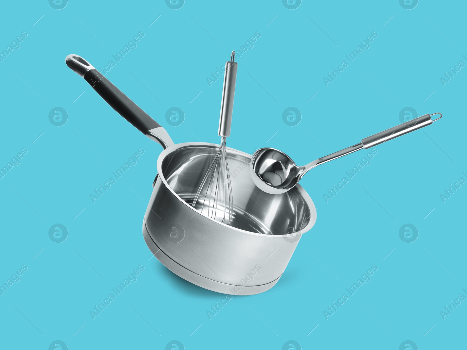 Image of Saucepan, ladle and whisk in air on light blue background