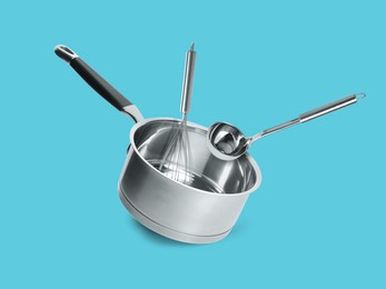 Saucepan, ladle and whisk in air on light blue background