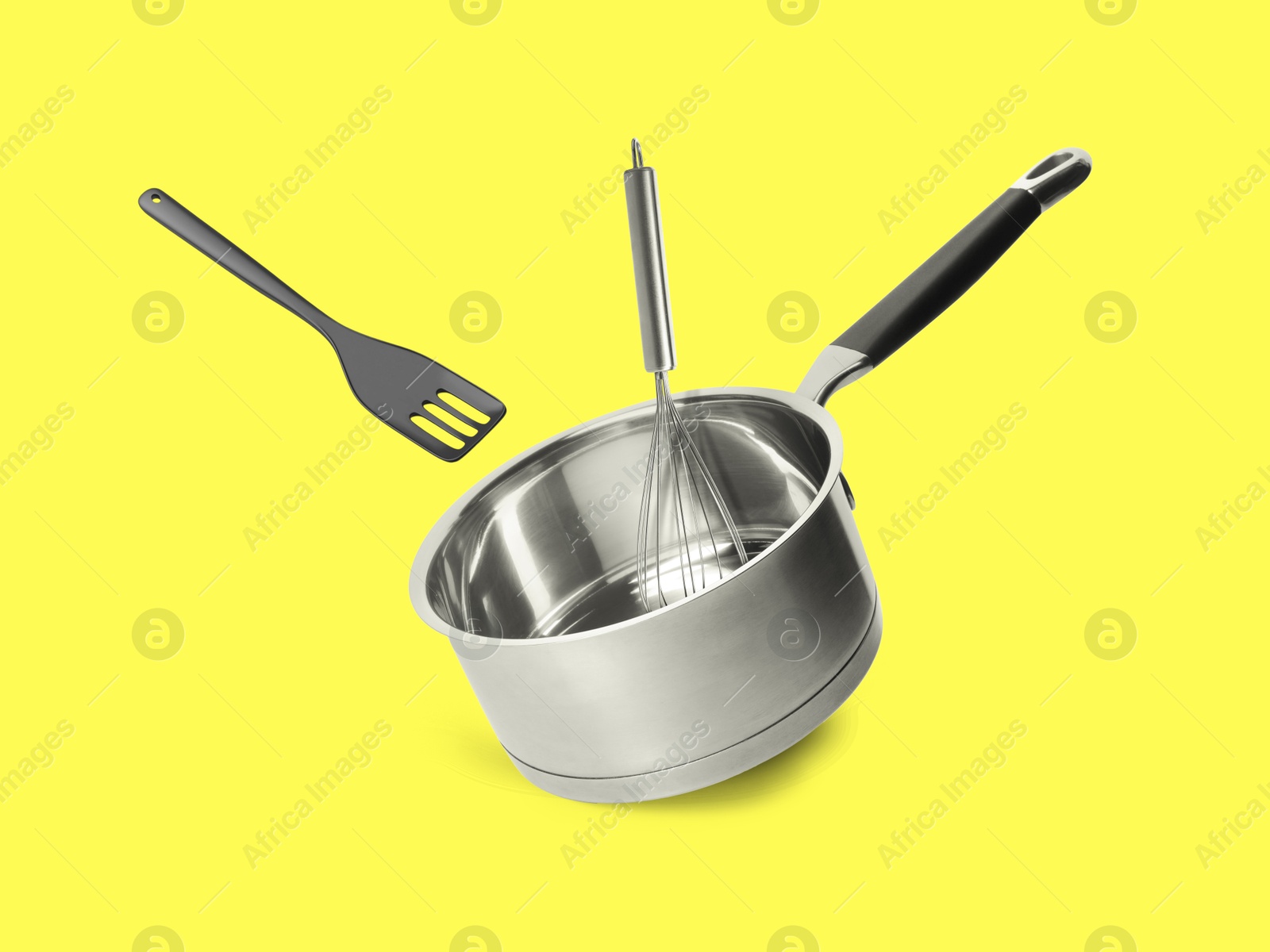 Saucepan, slotted spatula and whisk in air on yellow background Image of Saucepan, slotted spatula and whisk in air on yellow background