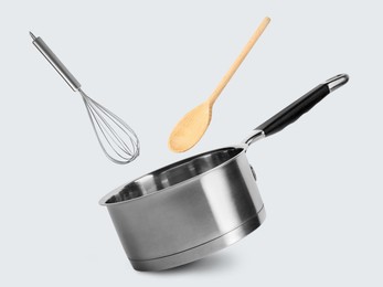 Image of Saucepan, whisk and wooden spoon in air on white background