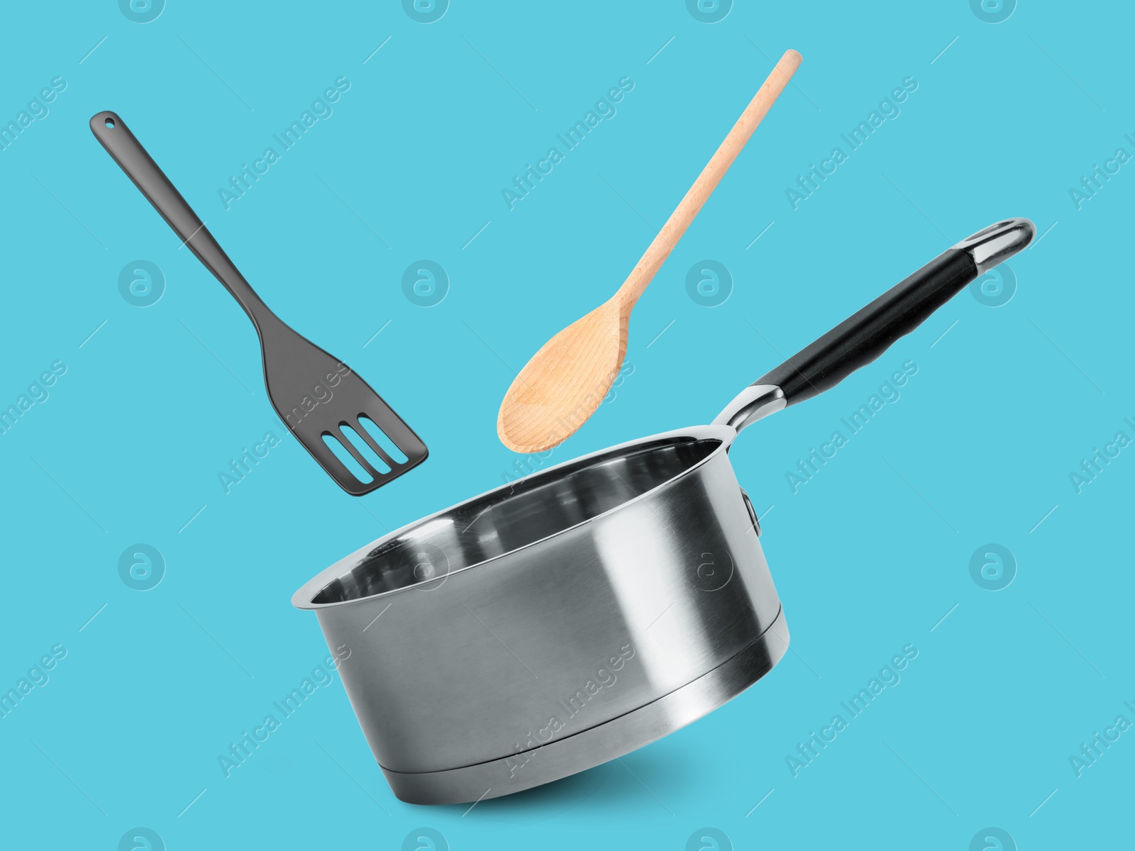 Image of Saucepan, slotted spatula and wooden spoon in air on light blue background