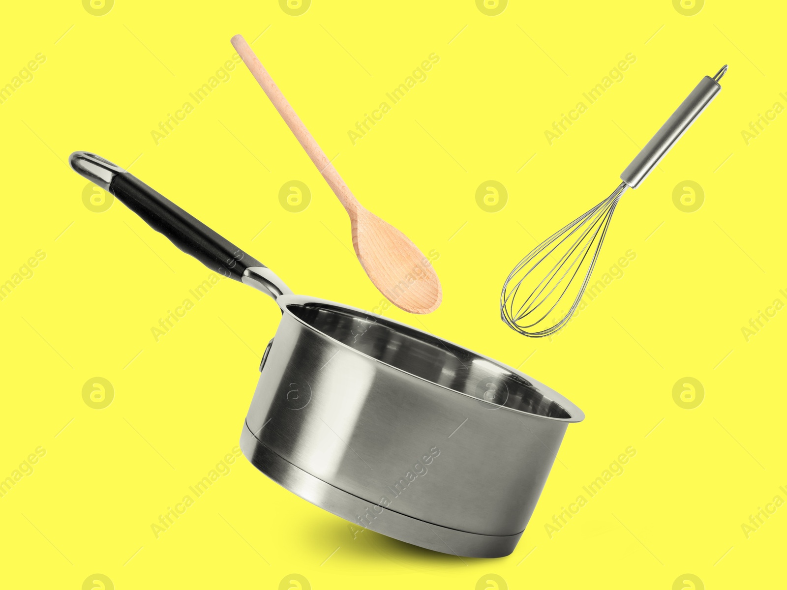 Saucepan, whisk and wooden spoon in air on yellow background Image of Saucepan, whisk and wooden spoon in air on yellow background
