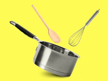 Image of Saucepan, whisk and wooden spoon in air on yellow background