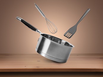 Image of Saucepan, whisk and slotted spatula in air on pale brown background