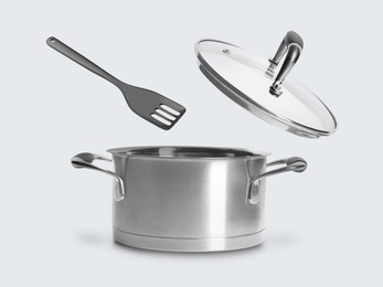 Slotted spatula and lid in air over saucepan on white background