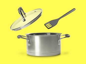 Slotted spatula and lid in air over saucepan on yellow background