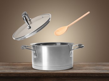 Image of Wooden spoon and lid in air over saucepan on table against pale brown background