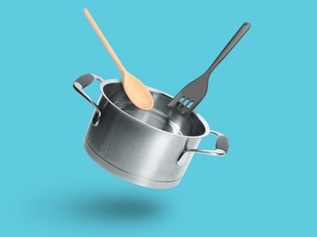 Image of Saucepan, wooden spoon and slotted spatula in air on light blue background