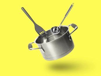 Image of Saucepan, ladle and slotted spatula in air on yellow background