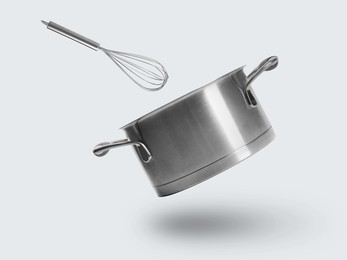 Saucepan and whisk in air on white background