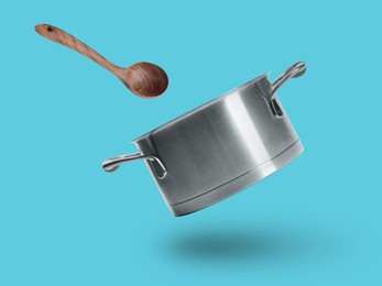 Image of Saucepan and wooden ladle in air on light blue background