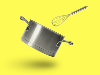 Saucepan and whisk in air on yellow background