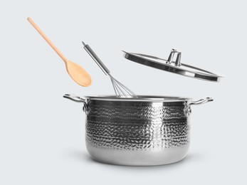 Image of Wooden spoon and whisk in air over saucepan on white background