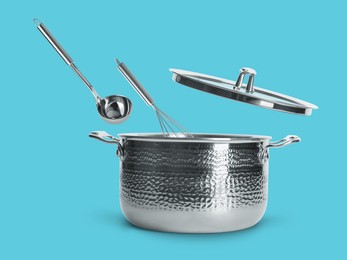 Image of Ladle and whisk in air over saucepan on light blue background