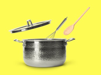 Image of Wooden spoon and whisk in air over saucepan on yellow background