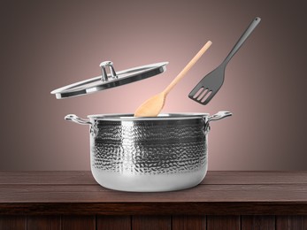 Image of Slotted spatula and spoon in air over saucepan on wooden table against pale brown background