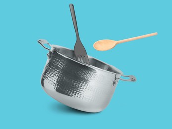 Image of Saucepan, wooden spoon and slotted spatula in air on light blue background