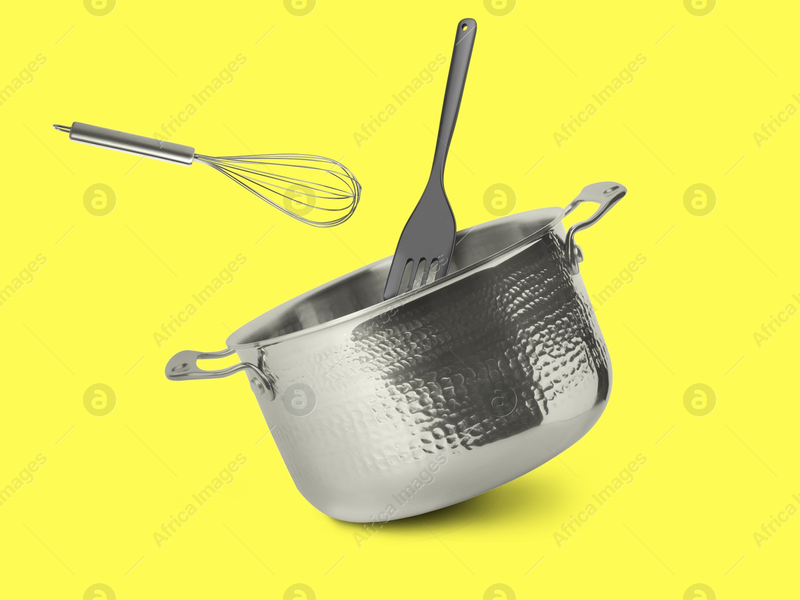 Image of Saucepan, whisk and slotted spatula in air on yellow background