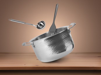 Image of Saucepan, ladle and slotted spatula in air on pale brown background