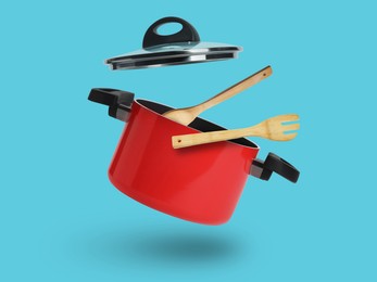 Image of Saucepan, wooden spoon and turner in air on light blue background