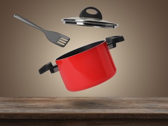 Saucepan and slotted spatula in air over wooden table against pale brown background