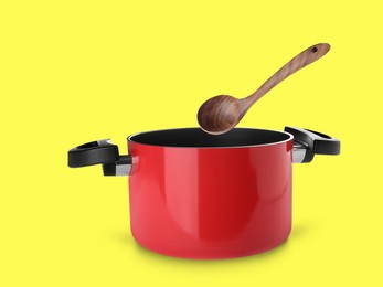 Image of Wooden ladle over saucepan on yellow background