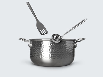 Image of Ladle and slotted spatula in air over saucepan on white background