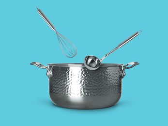 Image of Ladle and whisk in air over saucepan on light blue background