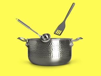 Image of Ladle and slotted spatula in air over saucepan on yellow background