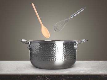 Image of Wooden spoon and whisk in air over saucepan on table against grey background