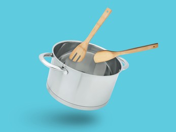 Image of Saucepan, wooden spoon and turner in air on light blue background