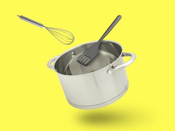 Saucepan, slotted spatula and whisk in air on yellow background