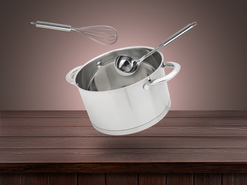 Saucepan, ladle and whisk in air on pale brown background