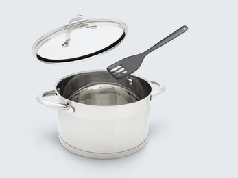 Slotted spatula and lid in air over saucepan on white background