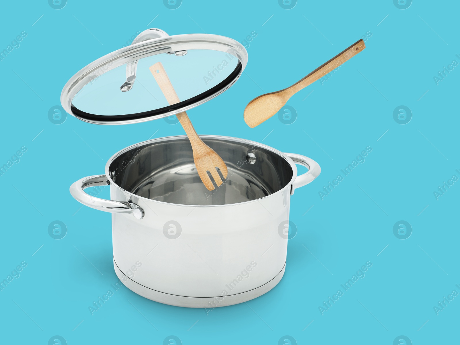 Image of Wooden spoon and turner in air over saucepan on light blue background