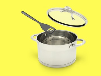 Slotted spatula and lid in air over saucepan on yellow background