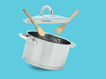 Image of Saucepan, wooden spoon and turner in air on light blue background