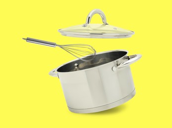 Image of Saucepan, whisk and lid in air on yellow background