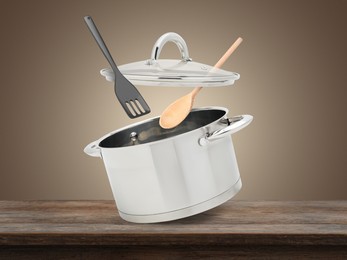 Image of Saucepan, slotted spatula and spoon in air on wooden table against pale brown background