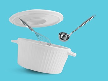 Saucepan, ladle and whisk in air on light blue background