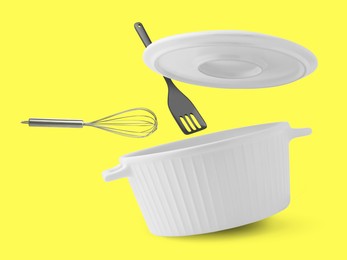 Saucepan, slotted spatula and whisk in air on yellow background